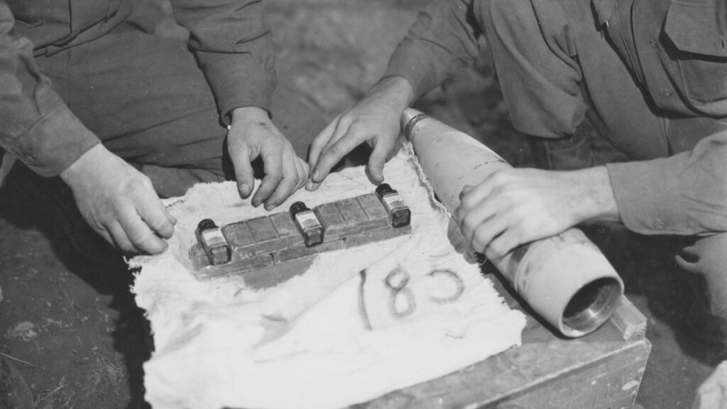 Soldiers of the 131st Field Artillery Battalion pack D-ration chocolate bars into hollow shell casings for delivery to a cut-off infantry battalion in France, Oct. 29, 1944.