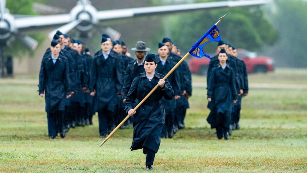 Air Force basic trainees marching behind a guidon at graduation
