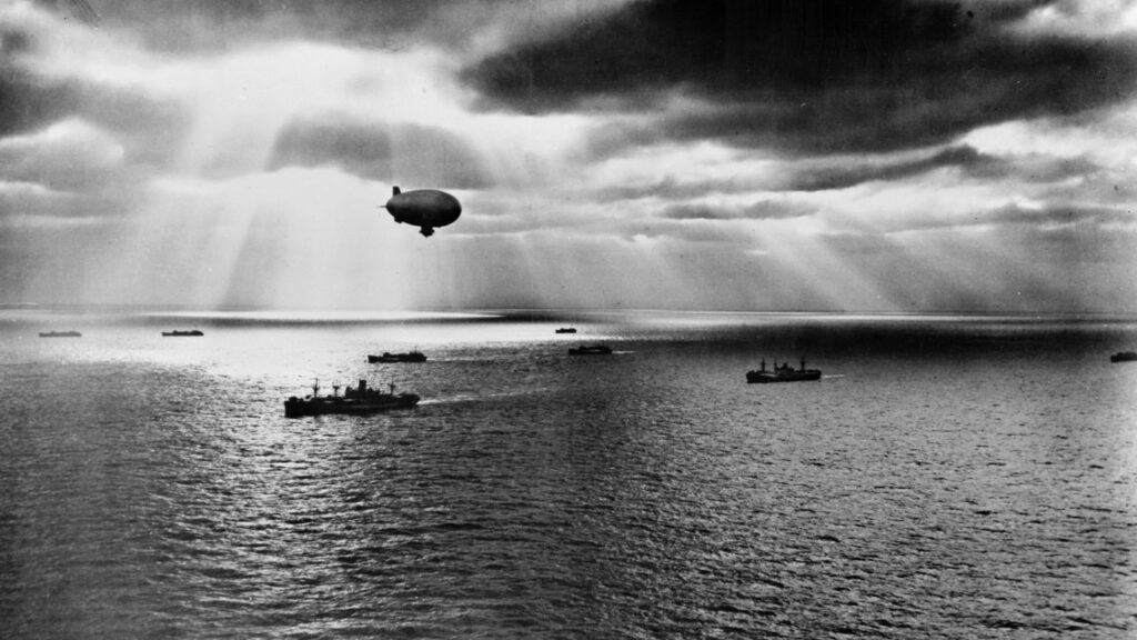 Navy blimp above a convoy of ships at sea