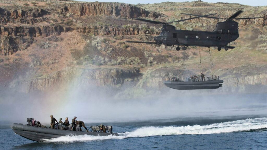 Navy special boat crew in a fast boat beneath a Chinook helicopter