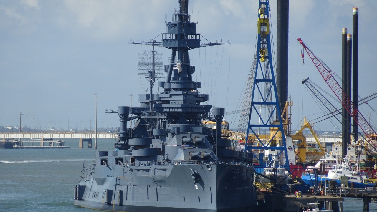Battleship Texas moored beside cranes at a shipyard in Galveston