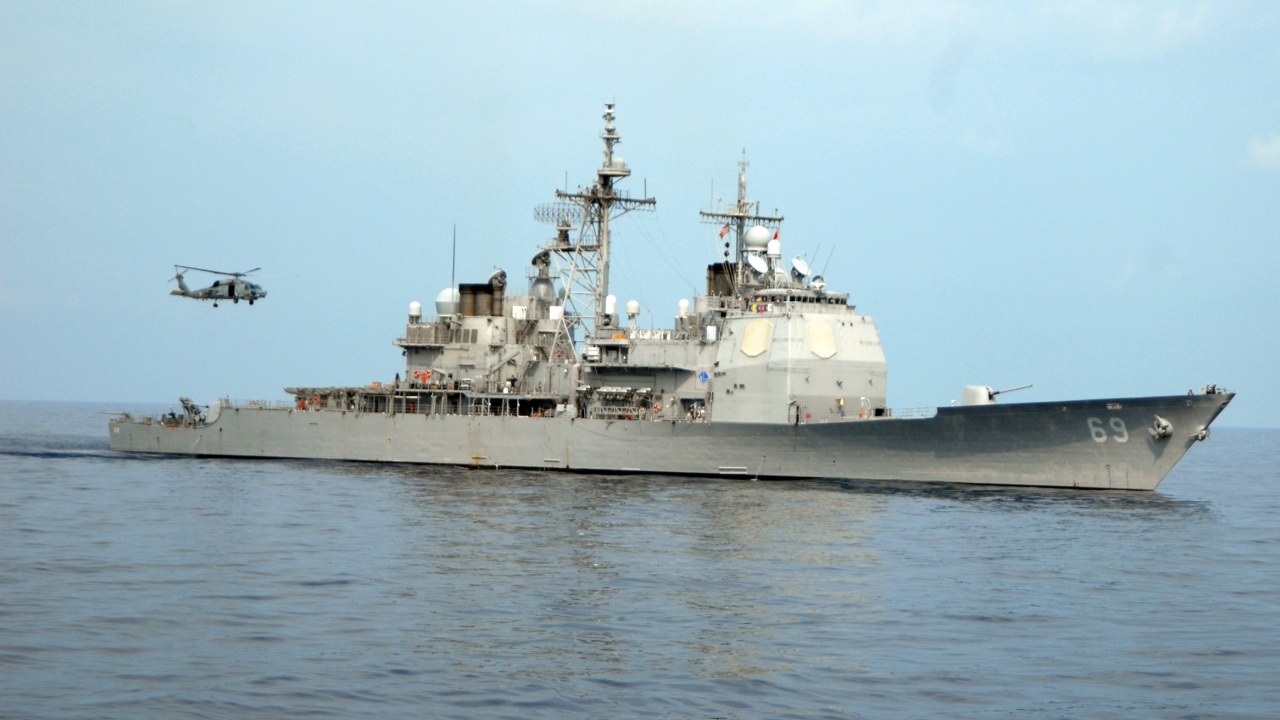 The cruiser USS Vicksburg underway with a helicopter overhead