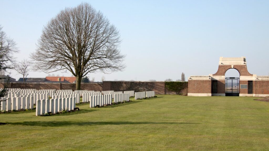 Rows of white headstones and the entrance gate at Poelcapelle British Cemetery
